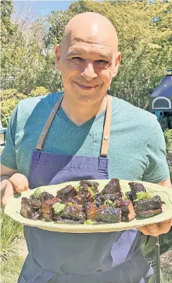  ??  ?? Chef Michael Symon with a plate of sticky ribs cooked low and slow on his new Food Network show “Symon’s Dinners Cooking Out.”