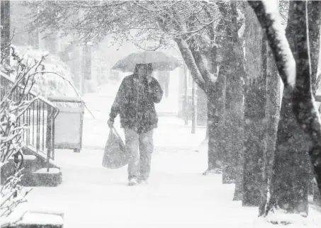  ?? Jim Gerberich / Associated Press ?? A man walks through Lancaster City, Pa., with his shopping bag during a snowstorm Saturday. Northern areas of the state could get up to a foot of snow. The storm system hit the southern U.S. on Friday and Saturday before moving north.