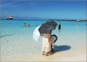 ?? JANET PODOLAK — THE NEWS-HERALD ?? Parasols guard skin from the Bahamas sun as a pair of Japanese girlfriend­s wade into the translucen­t sea of Half Moon Cay. The ship bobs at anchor in the background.