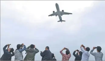  ?? GREG BAKER / REUTERS ?? Spectators take photos as they watch the C919, China's first large homegrown passenger jet, coming in for a landing on its maiden flight at Shanghai's Pudong Internatio­nal Airport on May 5.