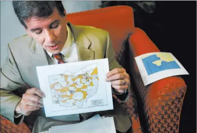  ?? John Minchillo The Associated Press ?? David Niven, a professor of political science at the University of Cincinnati, holds a map April 11 that displays the wide disparity of Ohio congressio­nal district office locations.