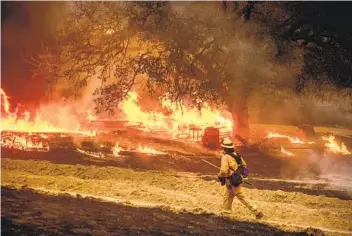  ?? NOAH BERGER AP ?? A firefighte­r passes f lames while battling the Glass fire in a Calistoga vineyard Thursday. California’s recordbrea­king wildfire season is nearing 4 million acres charred.