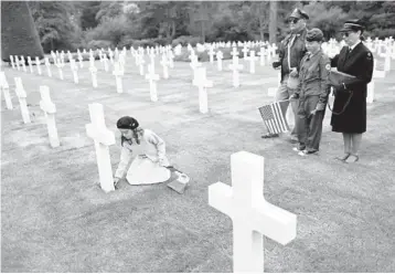  ?? JEREMIAS GONZALES/AP ?? A girl named Alice places a flower by a headstone while members of her family look on Saturday at the Normandy American Cemetery in Colleville-sur-Mer, France. Several ceremonies are scheduled to take place on Monday to mark the 78th anniversar­y of D-Day, which led to the liberation of France and other European countries in World War II.