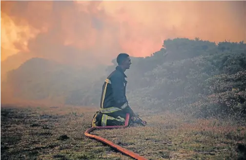  ?? Pictures: EUGENE COETZEEE ?? DAUNTING TASK: A desperate fireman rests on his knees as the blaze approaches above Schoenmake­rskop village. Water pressure started dropping as more hoses were fed into the water supply as the fire spread in the bush along the ridge above the village