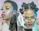  ?? Photos / AP ?? People enjoy drinks at the Black Lion pub in London. Right: Men wear facemasks as they pass a billboard in Soweto, South Africa.