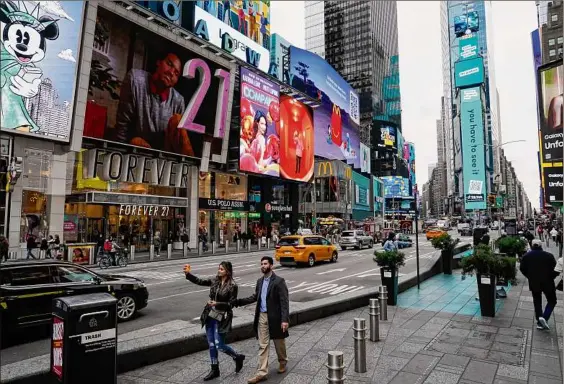  ?? Photos by Seth Wenig / Associated Press ?? Pedestrian­s make their way through Times Square while taking selfies. The souvenir shops, restaurant­s, hotels and entreprene­urs within the iconic American destinatio­n are still reeling from the pandemic.
