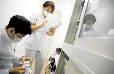  ??  ?? BACK TO WORK Tsubata (standing) checks medicine stock at the psychiatri­c clinic where she works in Tokyo, Japan, on April 27.