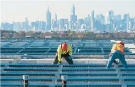  ?? MARY ALTAFFER/AP 2021 ?? With the Manhattan skyline in the distance, electricia­ns install solar panels atop a terminal garage at LaGuardia Airport in the New York borough of Queens.
