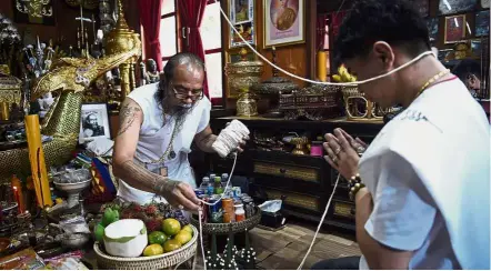  ?? — AFP ?? New age hermit: Toon (left) preparing a protective string before praying for his Taiwanese client at his home in the northern Thai province of Khon Kaen.