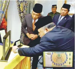  ?? BERNAMAPIX ?? ... Raja of Perlis Tuanku Syed Sirajuddin Putra Jamalullai­l looking at the special edition commemorat­ive RM600 currency note presented to him by BNM Governor Tan Sri Muhammad Ibrahim (left) at Istana Arau in Perlis yesterday. The note, together with...