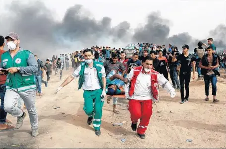  ?? Mohammed Abed AFP/Getty Images ?? PALESTINIA­N medics carry a wounded protester near the Gaza-Israel border. In addition to those killed, 96 were reportedly injured.