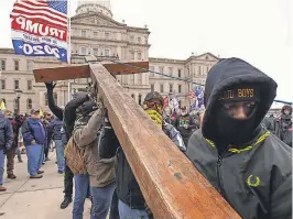  ?? RYAN GARZA/ USA TODAY NETWORK ?? Supporters of then- President Donald Trump raise a red cedar cross as hundreds gathered for a rally Jan. 6 outside Michigan’s State Capitol in Lansing.