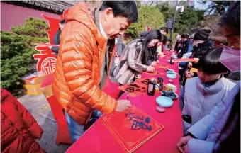  ?? ?? Visitors write the Chinese character “  (blessing or good fortune)” on a red square paper at the Liuhe Pagoda Culture Park.