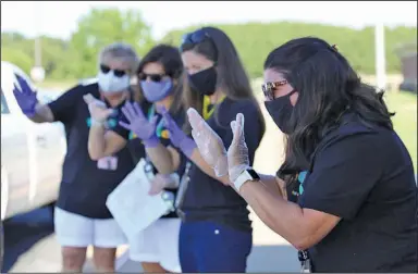  ?? (NWA Democrat-Gazette/Dan Holtmeyer) ?? Art teacher Olivia Slone (right) and other teachers at Tucker Elementary School in Lowell wave to students and their families Thursday during a back-to-school drive-thru event to deliver school supplies and meet one another. Staff members and students will wear masks when school begins Monday and take unmasked outdoor breaks throughout the day. It’ll be a challenge to keep young kids masked, Slone said, but “we’ll do our best.” More photos available at nwaonline.com/823masks/.