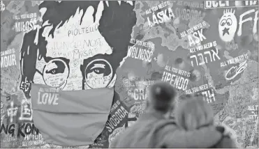  ?? Ap-petr david Josek, File ?? A couple look at the “Lennon Wall” with a face mask attached to the image of John Lennon, in Prague, Czech Republic. Like so many other events in the year of coronaviru­s, an annual tribute to John Lennon held in its adopted city of New York will go online. The five-hour event will be streamed for free on Lennon’s birthday, Oct. 9, starting at 7 p.m. on the LennonTrib­ute.org website.