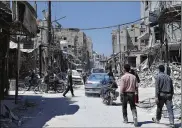  ?? HASSAN AMMAR / AP ?? People walk among damaged buildings in Douma, the site of a suspected chemical weapons attack, near Damascus in April. Clashes between the army and rebels have intensifie­d in recent days.