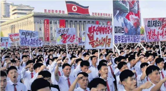  ??  ?? > Tens of thousands of North Koreans at a rally at Kim Il Sung Square carrying placards and propaganda slogans. Propaganda poster second from right says ‘American imperialis­ts, dare not run wild!’