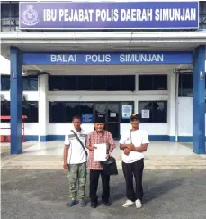  ??  ?? Aju (centre) holds up the report at the Simunjan district police headquarte­rs.