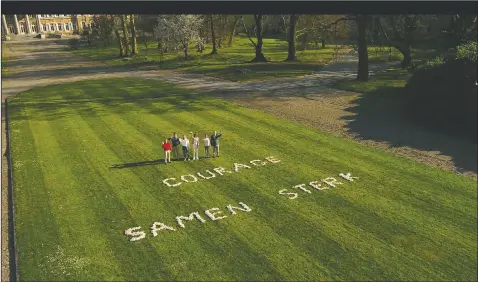  ?? (VTM) ?? Belgium’s King Philippe (right) stands with members of his family in the Royal Gardens of Laeken with a message ‘Courage, strong together’ written on the lawn on April 4. In a pandemic time rife with restrictio­ns, demands to respect social distancing have become quasi impossible to respect in public parks. One family in town though, has a lush garden all its own and ever more voices are being raised that the Royal Family of King Philippe should loosen up and open up at least part of their Park of Laeken to the public.