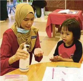  ?? PIC BY MOHD FADLI HAMZAH ?? A teacher showing a preschoole­r how to use hand sanitisers at Tabika and Taska Kemas Bunga Raya in Putrajaya yesterday.