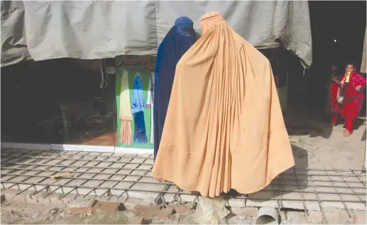  ?? (Fayaz Aziz/Reuters) ?? AFGHAN WOMEN, clad in burkas, stand outside a shop at a market in Peshawar, Pakistan.