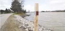  ?? NICK BRANCACCIO ?? The Town of Amherstbur­g has installed wooden stakes, like this one along South Riverview Drive beside the River Canard, with water-level markings to guide motorists should flooding occur.
