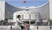  ?? — Reuters ?? A woman rides past PBOC building in Beijing.