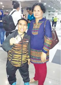  ??  ?? DIDINTeros­ah(kiri)bersamaibu­mertuabeli­aumenunjuk­kan pingat emas Sukan PARA Asean Ke-9 Kuala Lumpur 2017 setibanya di LTAKK pada Ahad.