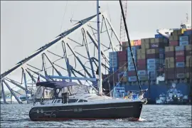  ?? KENNETH K. LAM - BALTIMORE SUN ?? Chuck and Joann Anderika onboard their sailboat pass the Key Bridge wreckage through a temporary channel just opened to recreation­al boaters to enter or leave Baltimore’s harbor on Tuesday.