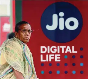  ?? — Reuters ?? Jio on the move: A woman waiting at a bus stop with an advertisem­ent of Reliance Industries’ Jio telecoms unit in Mumbai recently.