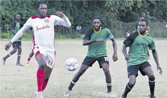  ?? (Photo: Paul Reid) ?? Wade Daley (left) of Cambridge FC goes after the ball as Reggae Youths players Sachin Dennis (centre) and Sebastian Robinson look on during Sunday’s first-leg semi-finals of the St James FA Sandals Resorts Internatio­nal Major League at the UDC field. Daley scored a hat-trick as Cambridge FC came from behind twice to win the game 3-2.