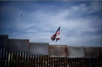  ?? RAMON ESPINOSA — THE ASSOCIATED PRESS ?? U.S. and California state flags fly behind the border wall, seen from Tijuana, Mexico, Monday. Tensions have built as nearly 3,000 migrants from a caravan poured into Tijuana in recent days after more than a month on the road — and with many more months likely ahead of them while they seek asylum in the U.S. The federal government estimates the number of migrants could soon swell to 10,000.