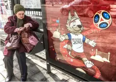  ?? — AFP photo ?? An elderly woman sits at a bus stop next to a poster featuring Zabivaka, the official mascot of the 2018 FIFA World Cup in downtown Moscow.