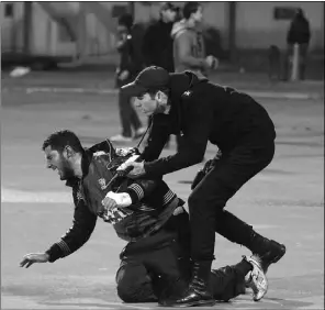  ??  ?? A policeman arrests an injured man as chaos followed a pitch invasion at a stadium in Port Said, in an incident one player described as “a war, not football.”