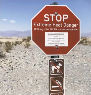  ?? Mario Tama / Getty Images ?? Visitors walk near a sign warning of extreme heat danger on Monday in Death Valley National Park, Calif.