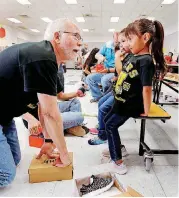  ??  ?? Hiromi Morales, a prekinderg­arten student at Wheeler Elementary School in Oklahoma City, gets help trying on shoes Friday from volunteer Dan Hester. About 400 students received a free pair of shoes courtesy of MetroShoe Warehouse.