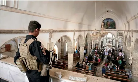  ?? AP ?? A Christian militiaman stands guard during mass in Qaraqosh, Iraq. Churches and other houses of worship are routinely at risk of attack in many parts of the Middle East.