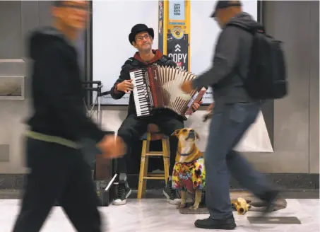  ?? Paul Chinn / The Chronicle ?? Robert Doerr plays the accordion, accompanie­d by his dog, Vera, for commuters at the Civic Center/U.N. Plaza BART Station.