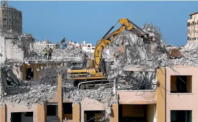  ?? AP ?? Palestinia­n workers use a backhoe to break and remove parts of the Al-Jawhara building that was damaged in Israeli airstrikes during Israel’s war with Gaza’s Hamas rulers last May.