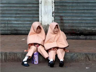  ??  ?? VULNERABIL­IDAD. Dos niñas vistiendo uniforme escolar se sientan en una acera mientras esperan la furgoneta que las llevará a su escuela en la localidad paquistaní de Karachi.