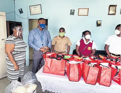  ?? CONTRIBUTE­D ?? Mark Barnett (second left), president of the Rotary Club of Downtown Kingston, along with a club member, speaks with students of schools in downtown Kingston during a handover of care packages recently.