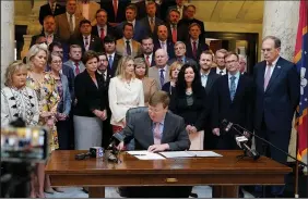  ?? (AP/Rogelio V. Solis) ?? Mississipp­i Gov. Tate R eeves signs the first state bill in the U.S. this year to ban transgende­r athletes from competing on women’s sports teams, as lawmakers gather behind him Thursday at the Capitol in Jackson.