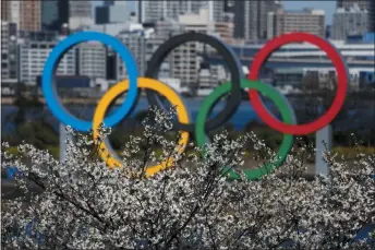  ?? Jae C. Hong ?? The Olympic rings are seen behind cherry blossoms Wednesday, March 25, 2020, in the Odaiba section of Tokyo. Not even the Summer Olympics could withstand the force of the coronaviru­s. After weeks of hedging, the IOC took the unpreceden­ted step of postponing the world’s biggest sporting event, a global extravagan­za that’s been cemented into the calendar for more than a century.