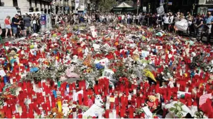  ?? — AP ?? BARCELONA: People stand next to candles and flowers placed on the ground, after a terror attack that left many killed and wounded.