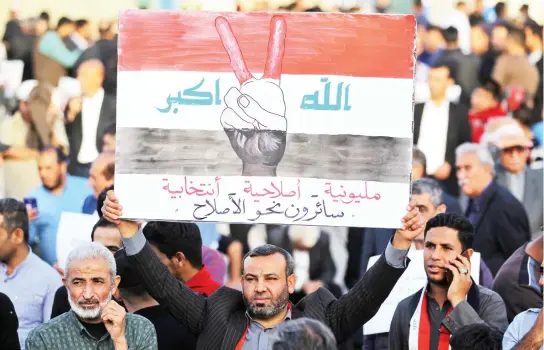  ??  ?? An Iraqi supporter of Moqtada Al-Sadr raises a sign showing the colors of the Iraqi flag superimpos­ed on a hand flashing the victory gesture with a caption in Arabic reading at the bottom ‘million-man march, reformist, electoral, walking towards...
