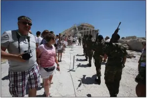  ?? (AP) ?? Tourists look on as members of Greece’s Presidenti­al Guard march past at the Acropolis in this file photo. The pandemic continues to take a toll on the country’s tourist industry as travel uncertaint­ies persist.