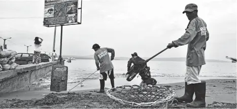  ?? MACKY LIM ?? LINIS DAGAT. Bantay Dagat personnel of Davao City scrape off trash buried in the sand at Sta. Ana Pier yesterday morning. The men, however, seem to be having difficulty digging in the sand as garbage is buried deep.