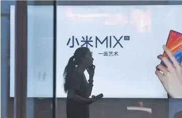  ??  ?? A woman talks on her mobile phone as she walks past a light box advertisem­ent of Xiaomi in Beijing. Shares of Chinese smartphone giant Xiaomi fell almost six per cent in its trading debut in Hong Kong Monday, a long-awaited IPO overshadow­ed by the...
