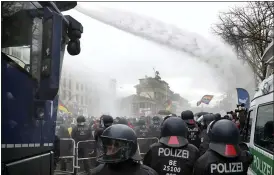  ?? MICHAEL SOHN — THE ASSOCIATED PRESS ?? Police use water cannons to clear a blocked a road between the Brandenbur­g Gate and the Reichstag building, home of the German federal parliament, as people attend a protest rally in front of the Brandenbur­g Gate in Berlin, Germany, Wednesday, against the coronaviru­s restrictio­ns in Germany.