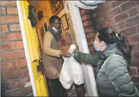  ??  ?? Volunteer Maria Martinez (right) hands bags of West Indian meals to Bridgette Toussaint prepared by members of the Preston Windrush Covid Response team in Preston, England.